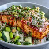 Fulfilled Bang Bang Salmon Bowl drizzled with creamy sauce and topped with fresh cucumber-edamame salsa served over fluffy rice.