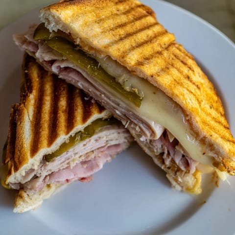 A crispy pressed Cuban sandwich stacked with roast pork, ham, and Swiss, served beside crunchy plantain chips.