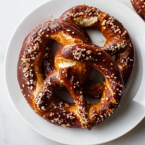 Eight warm Soft Pretzels lined up on a cooling rack, boasting a chewy interior and shiny, brown crust.