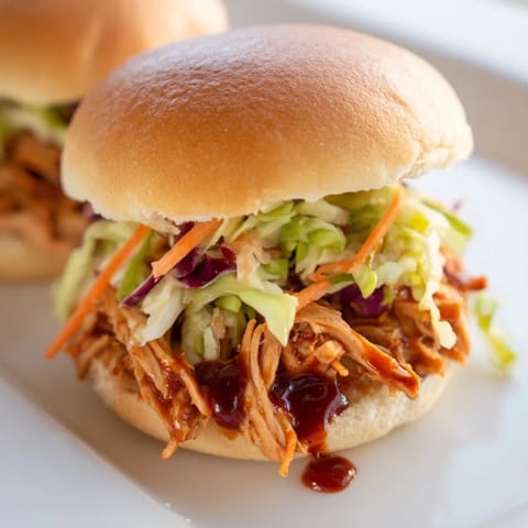 Golden BBQ chicken sliders with crunchy slaw on toasted mini buns, ideal for parties.  
