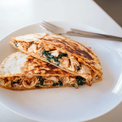 Golden-brown Chicken and Spinach Quesadilla wedges filled with melted mozzarella, resting on a plate beside a small bowl of sour cream.