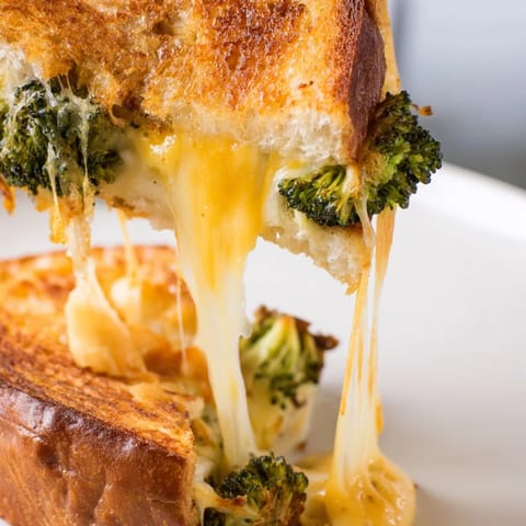 Golden toasted bread overflowing with melted sharp cheddar and caramelized roasted broccoli florets, served on a white plate.