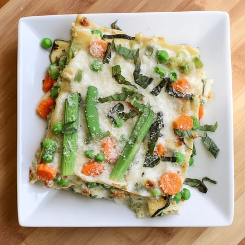 In a white baking dish, golden-bubbly Spring Veggie Alfredo Lasagna reveals tender peas, spinach, and zucchini between silky noodles.