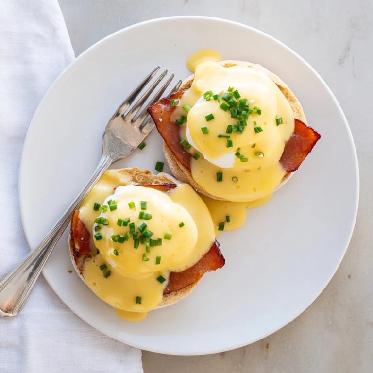 A perfect brunch presentation of Eggs Benedict topped with hollandaise and fresh chives.
