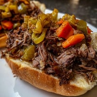 Freshly shredded Italian Beef Sandwich piled high on a toasted roll with spicy giardiniera and roasted peppers.