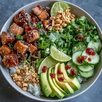 Flaky marinated salmon and creamy avocado slices rest on seasoned sushi rice for an Avocado Salmon Bowl, finished with chili oil and chopped peanuts.